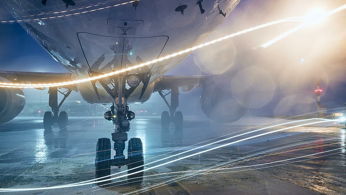Winter night at airport during snowfall. Streams of light are flowing underneath an airplane.