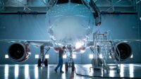 New airplane standing in an aircraft maintenance hangar while maintenance engineers and technicians go inside the cabin via a ladder.