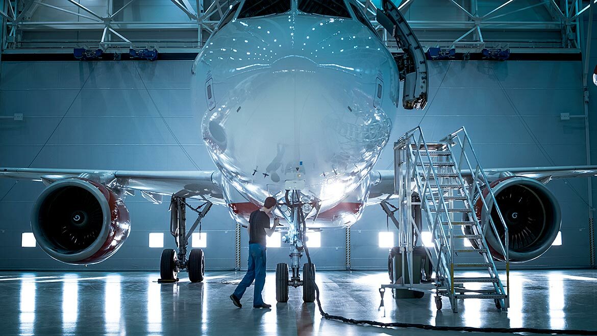New airplane standing in an aircraft maintenance hangar while maintenance engineers and technicians go inside the cabin via a ladder.