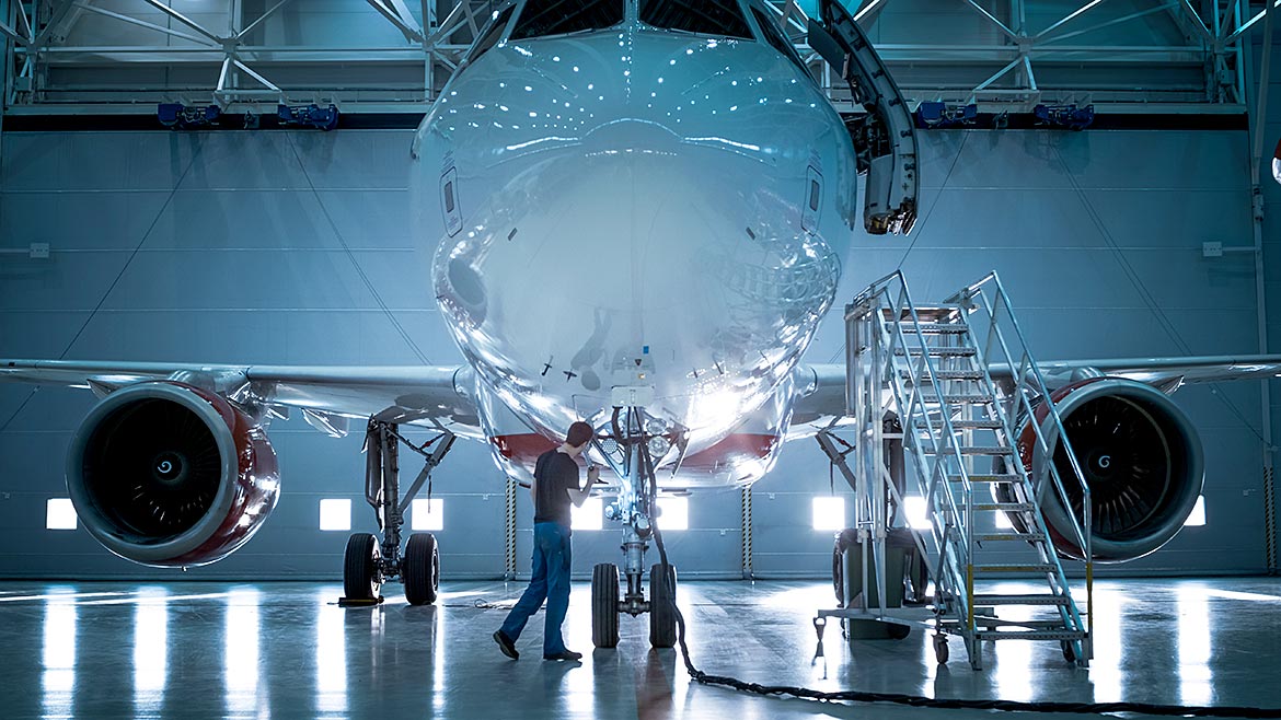 New airplane standing in an aircraft maintenance hangar while maintenance engineers and technicians go inside the cabin via a ladder.