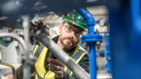 Manufacturing professional analysing machines. Manual worker is looking at pipe. He is in reflective clothing.