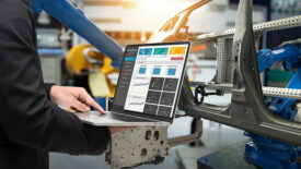 The male manager's finger is on a laptop checking real-time production monitoring system application in a smart factory industrial.