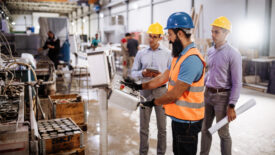 Engineers in factory hall, performing quality control. Manufacturing occupation in modern industrial hall, with automated process and robots. Metal processing industry and warehouse.