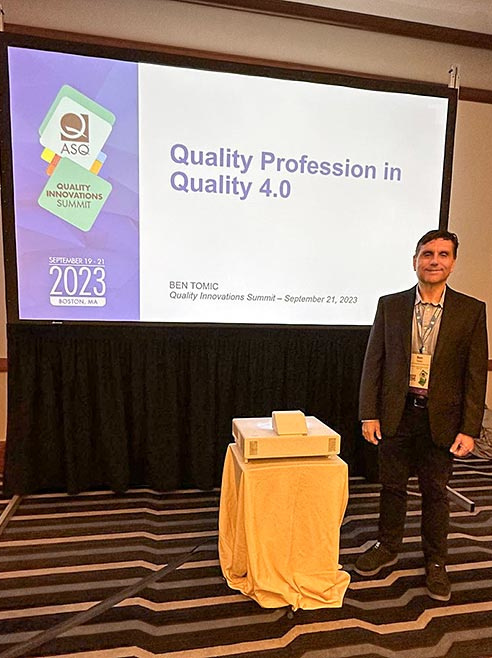 Ben Tomic posing in from of a projection at the2023 ASQ Boston.
