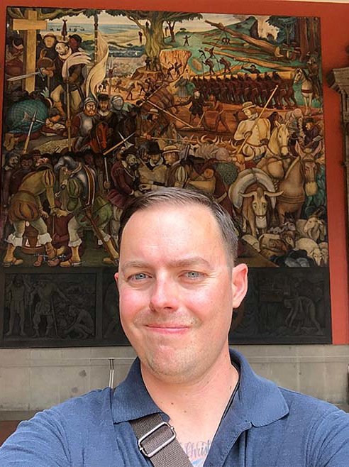 Justine Wise posing in front of a Diego Rivera mural: The Arrival of Cortés, Palacio Nacional de Mexico Diego Rivera 1951.