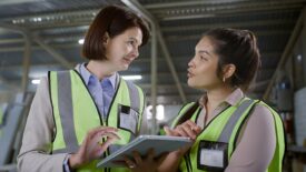 Engineering women using a tablet and having a discussion at a warehouse.
