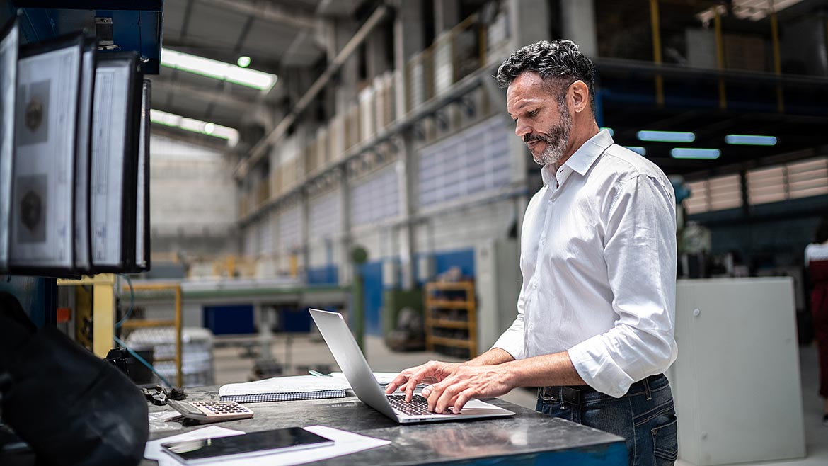 Mature businessman using laptop in a factory.
