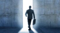 Businessman walking into bright light from inside building.